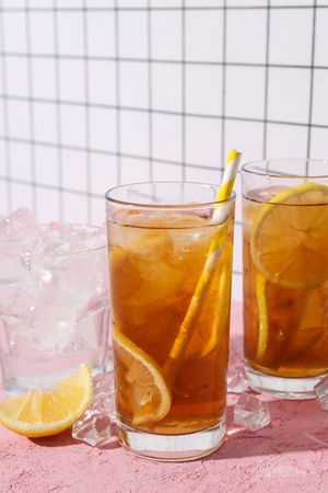A glass of cold tea with ice and an orange on a pink background