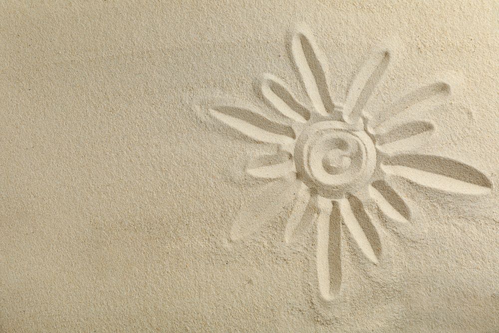 Sun drawing on clear sea sand, space for text and top view. Summer vacation background