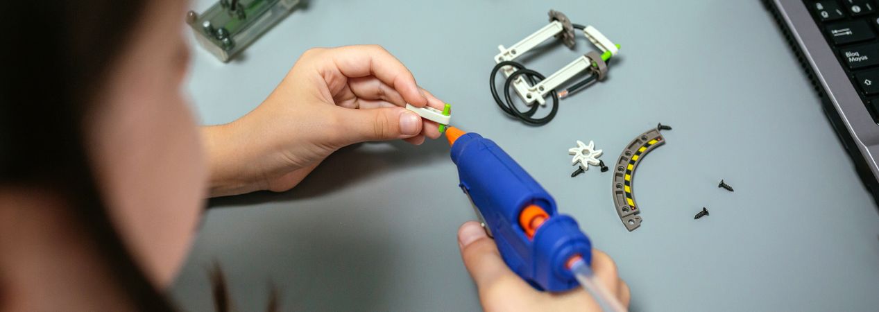 Student using hot melt glue gun on machine pieces in robotics class