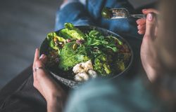 Woman in t-shirt and jeans sitting with fork in vegetarian bowl, top view