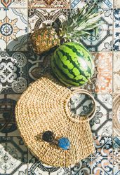 Thatched bag on pattered tiles with sunglasses, watermelon and pineapple, with shadows