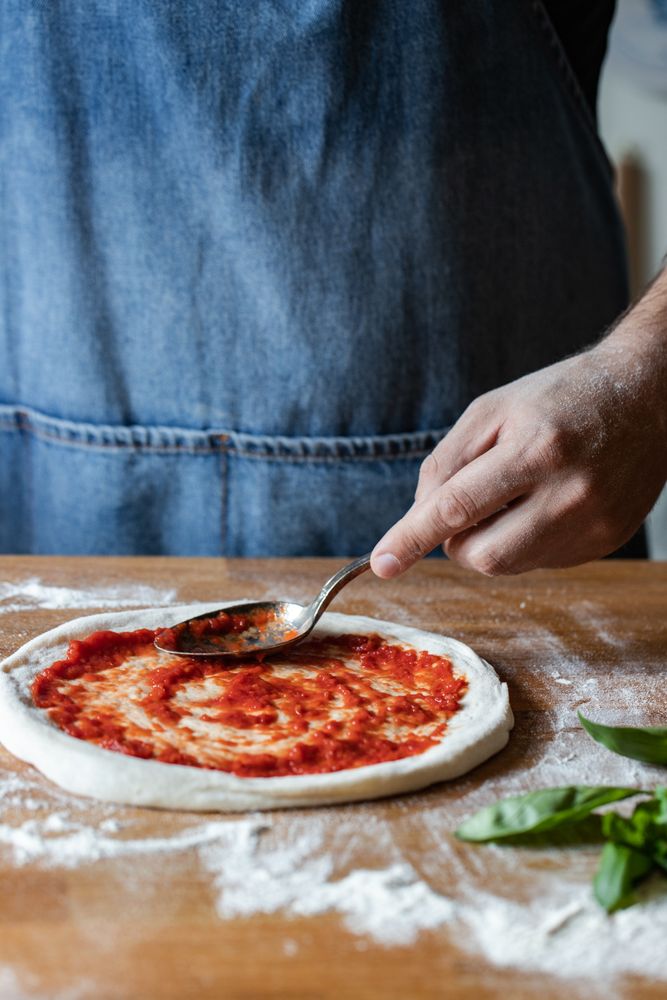Crop man spreading sauce on pizza dough