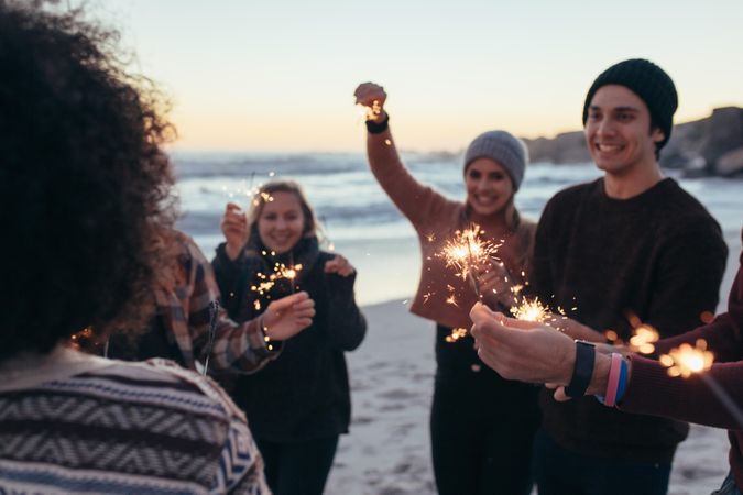Young people having fun with sparklers outdoors at the sea shore