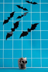 Bats flying above a ceramic skull glass on blue background