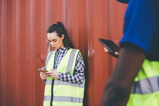 Woman in high visibility vest checking phone on site