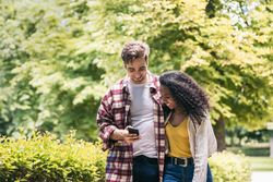 Happy multiracial couple taking a walk in the park using smartphone