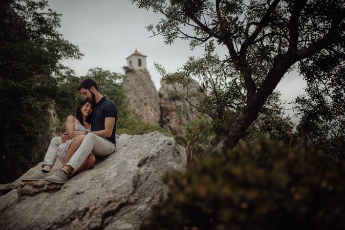 Romantic couple resting on rock surrounded with trees