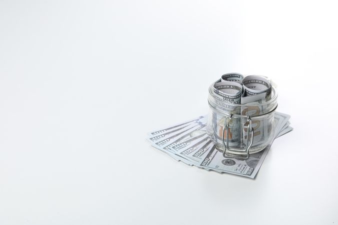 Stacks of American cash money in glass jar on light background, space for text