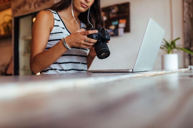 Woman blogger looking at her DSLR camera while working on her laptop computer at home