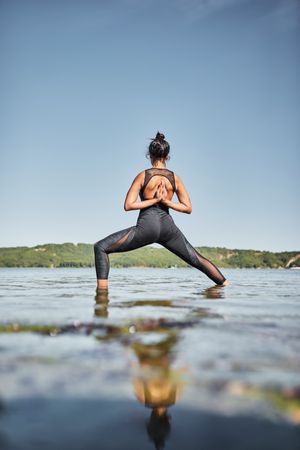 Rear view of young woman doing reverse prayer yoga pose in shallow lake water