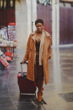 Stylish Black woman with luggage walking on street