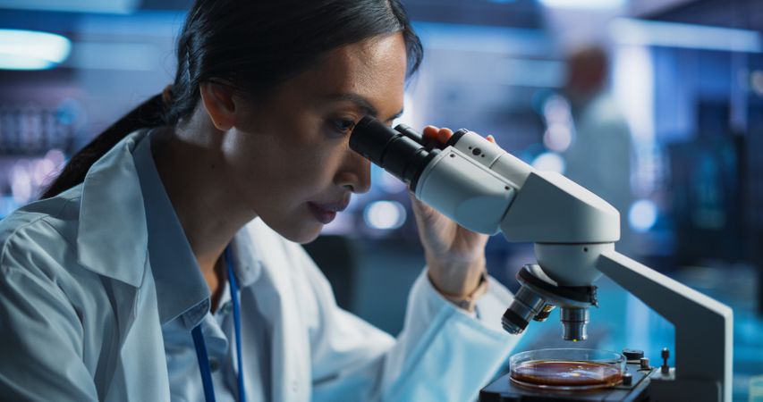 Medical Development Laboratory: Portrait of Asian Female Scientist Using Microscope, Analyzes Petri Dish Sample.