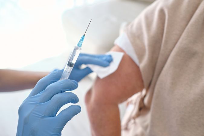Crop nurse with syringe preparing patient for vaccination