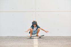 Cheerful child in VR glasses riding skateboard in city