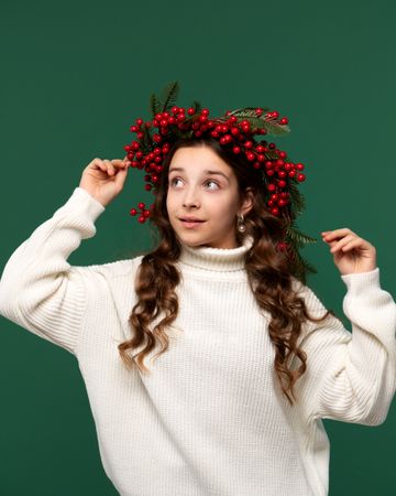 Girl adjusting red berry wreath, looking up curiously.
