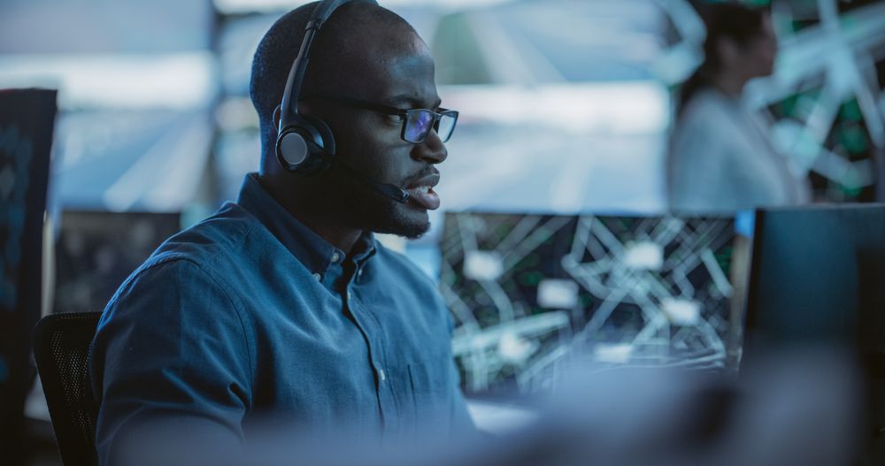 Black Man Effectively Multitasking with Supporting Clients on a Phone Call and Computer Work.