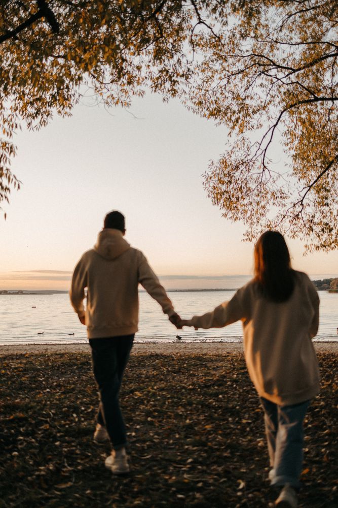 Back view of man and woman in light sweaters walking on beach at sunset
