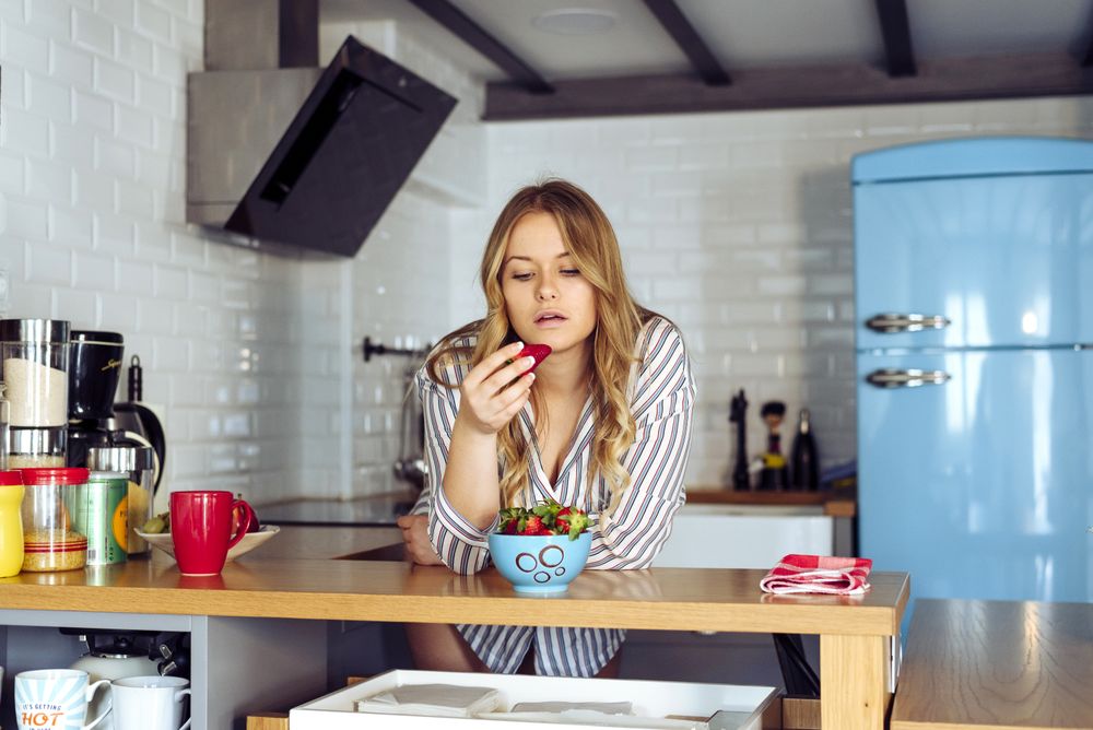 Young seductive female eating strawberry in kitchen