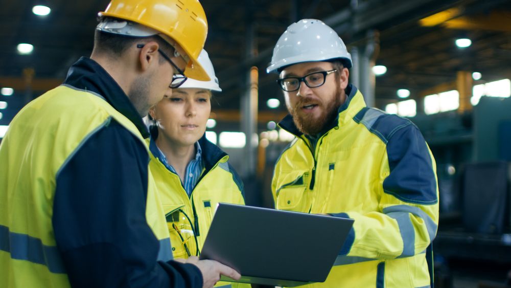 Three Industrial Engineers Talk with Factory Worker while Using Laptop.