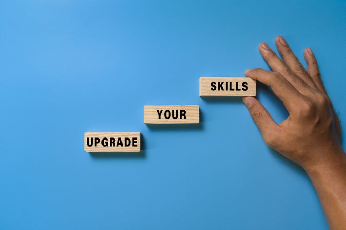 male hand put wooden blocks with upgrade your skills words isolated on blue background