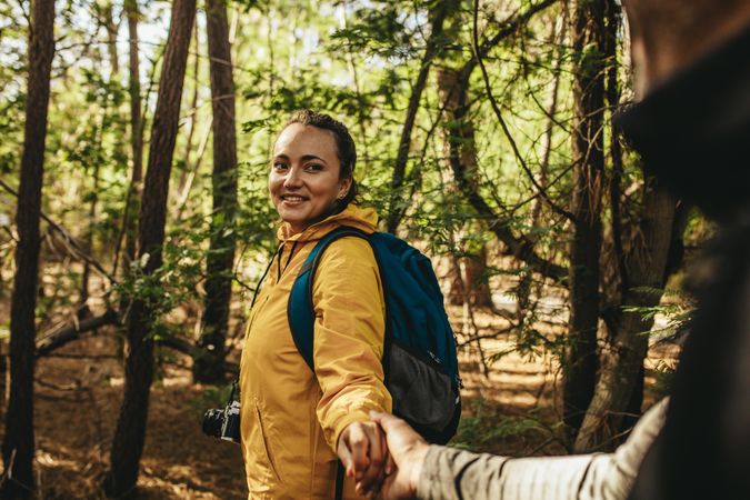 Woman holding man’s hand while hiking in a forest