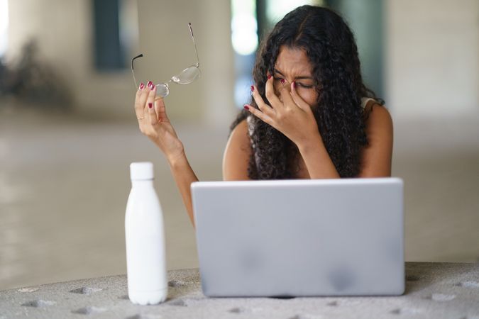 A Frustrated Woman Struggling to Work on Her Laptop While Holding Glasses in Her Hand