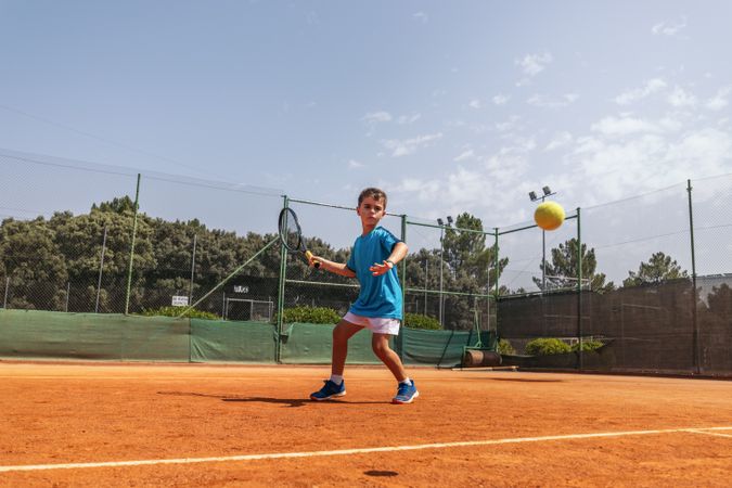 Little boy playing tennis on a dirt court