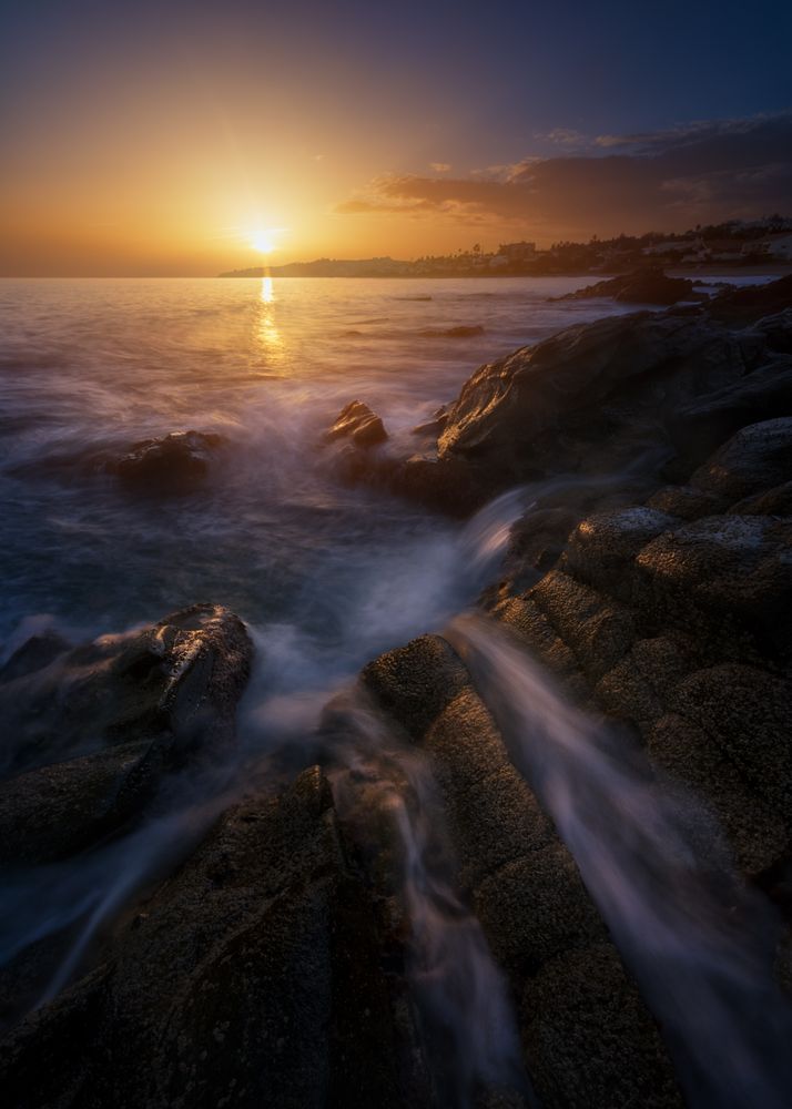 Sea waving near rough rocks during sunset