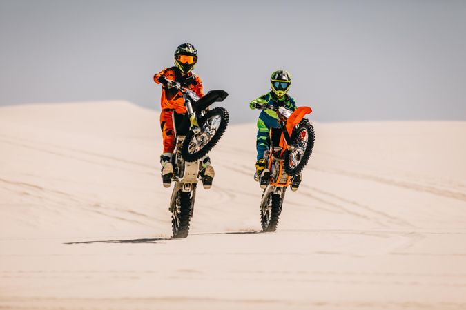 Skillful stunt bikers riding motorcycle on one wheel in desert