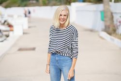 Older woman in jeans and striped shirt standing outside on sunny day