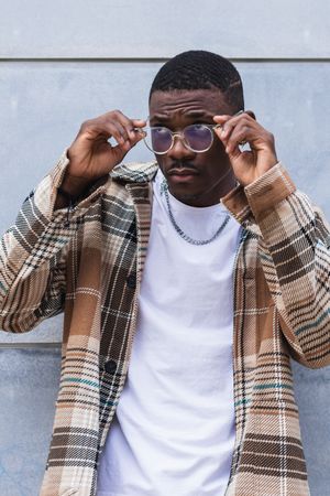 Stylish Black male standing near wall and putting on glasses