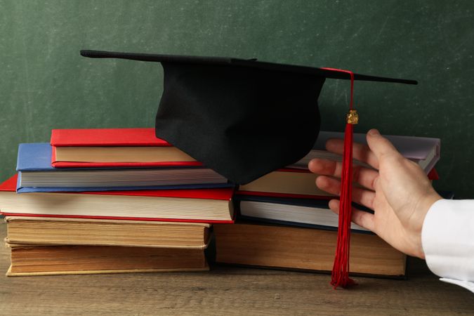 Graduation hat with books on a table on a dark background.