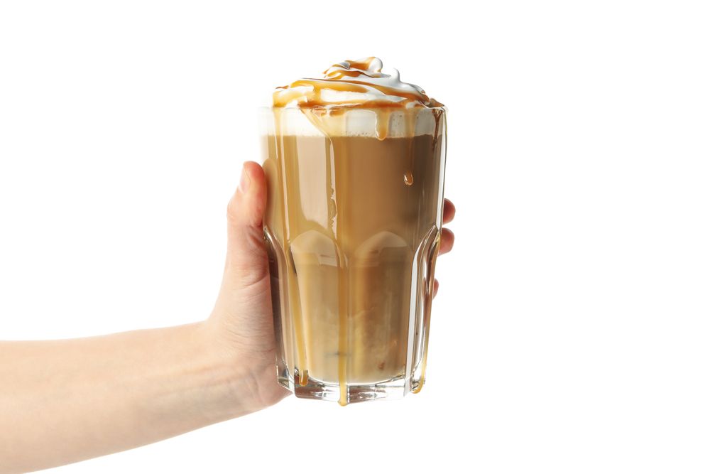 Female hand holds iced coffee with poured cream isolated on plain background