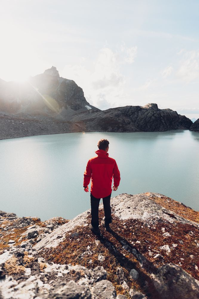 Back view of man in red jacket standing on waterside of frozen lake during daytime