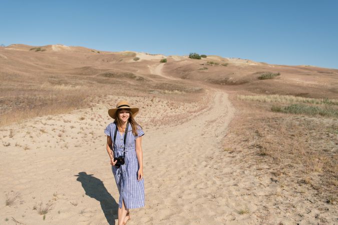 adult woman in straw hat and dress with camera walking on country path