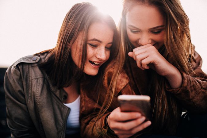 Two young women laughing at something on the phone