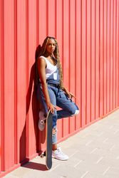 Woman leaning against red wall with skateboard, vertical composition with copy space