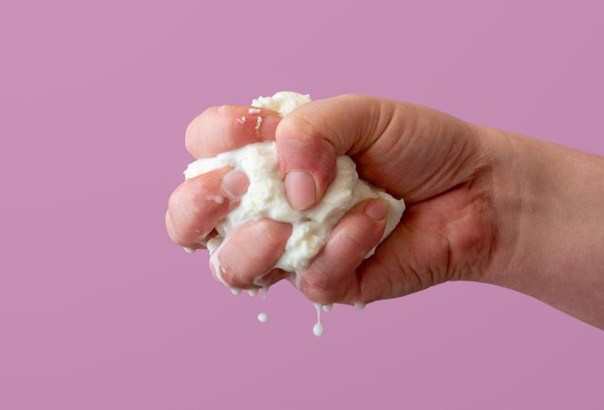 Squeezing mozzarella cheese in one hand, isolated on a purple background