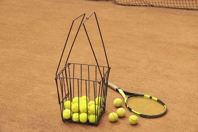 Racket and basket with balls on clay court