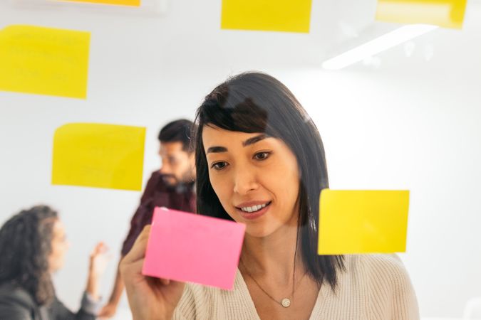 Asian woman writing on sticky notes brainstorming ideas from company meeting in coworking space