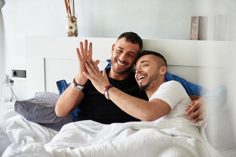 Smiling gay couple hugging on bed