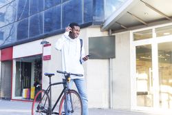 Young Black man walking in the street with bike and adjusting his headphones