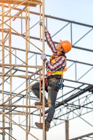 Man in orange bump cap climbing a scaffolding