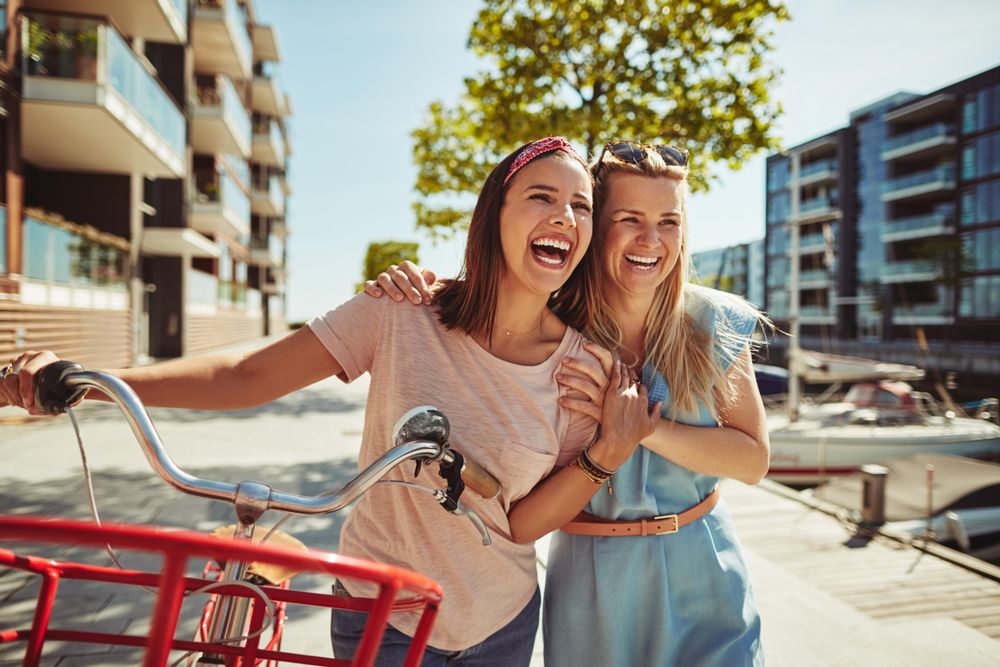 Two women smiling and walking with bicycle, close up