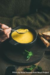 Man eating warm yellow soup from dark bowl with toast 5zjnn5