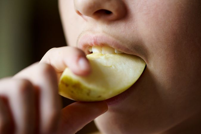Teenage girl biting into slice of apple