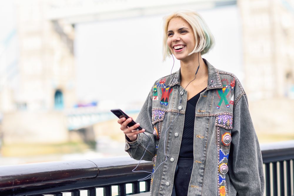 Joyful blonde female listening to music on phone along river walk