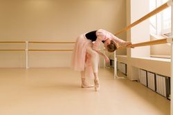 Ballet dancer leaning on barre, stretching in pink tutu