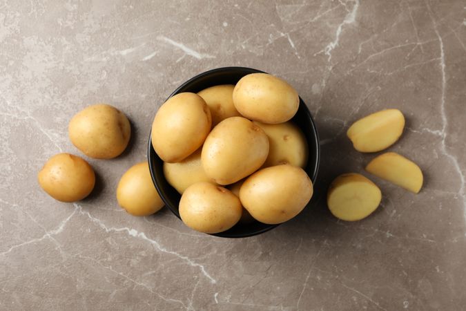 Top view of dark ceramic bowl overflowing with potatoes on marble counter