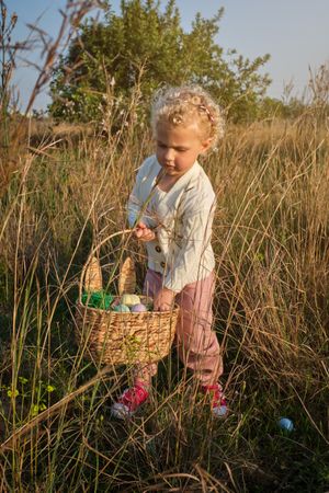 Cute girl collecting Easter eggs in sunny nature